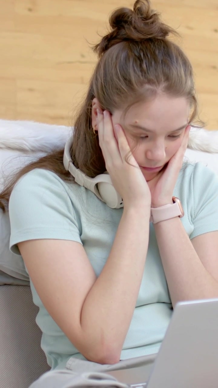 Video verticale: Schermo di laptop che mostra una donna con il viso tra le mani, appoggiata sul letto, che indossa una maglietta azzurra