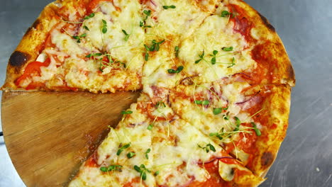 tasty pizza in restaurant. fresh round pizza with cheese and green sprouts on top rotating on a wooden board on a table. ready pizza without one part portion. close-up.