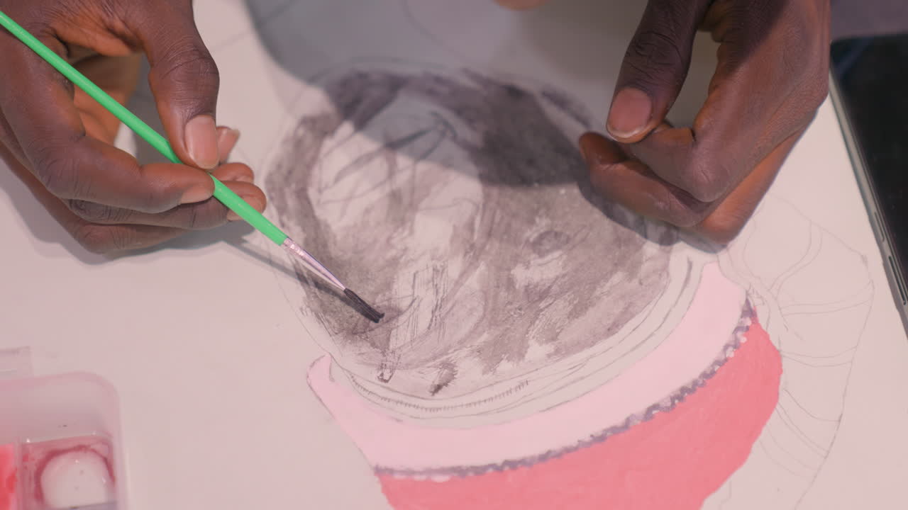 Overhead hands applying black painting wash with green brush, black student practices dynamic brush strokes and charcoal smudging, lively studio vibe with closeup motion, palette and tools visible