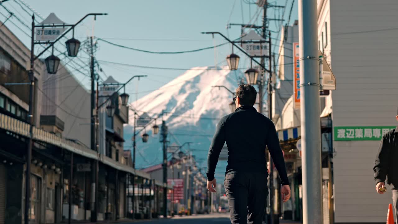 un clip cinematográfico que captura a un hombre paseando por la calle honcho en la ciudad de shizuoka, con el icónico monte fuji en el fondo, cubierto de nieve.
