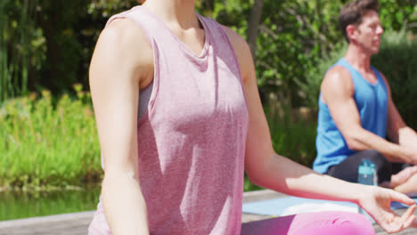 diverse male and female group practicing yoga sitting on mats with eyes closed in sunny park