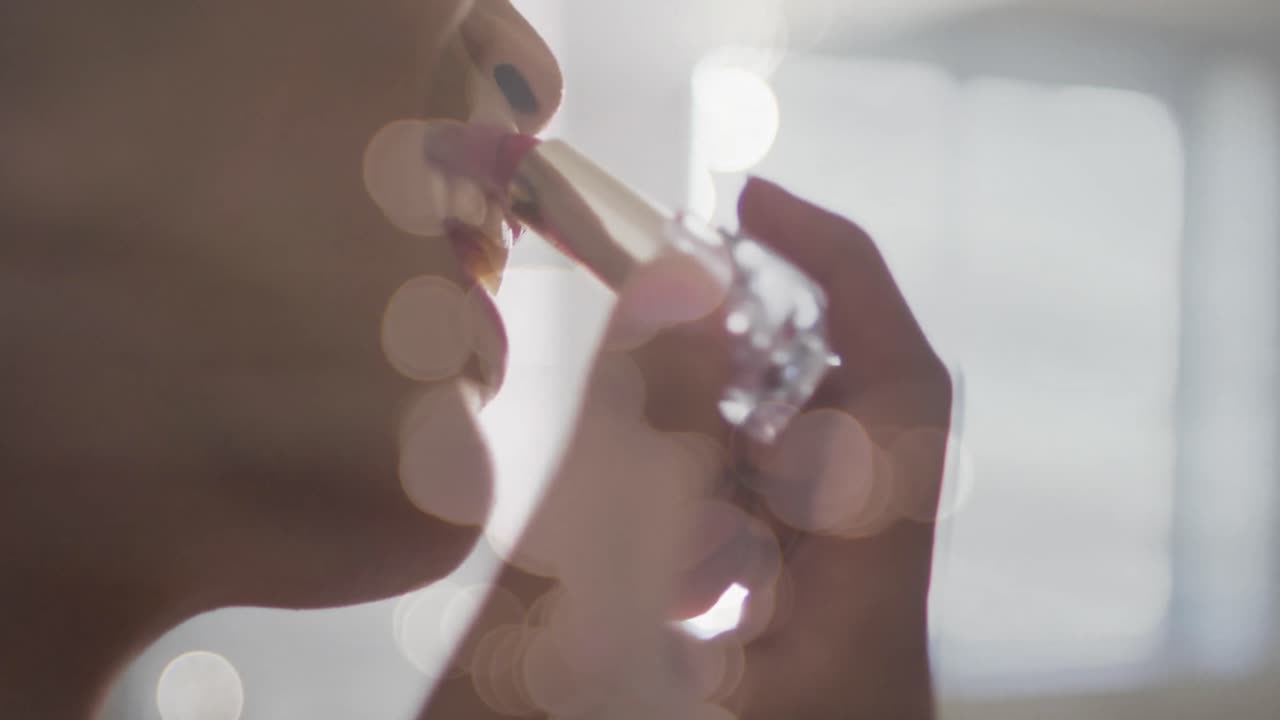 animación de manchas de luz sobre una mujer biracial aplicando lápiz labial.