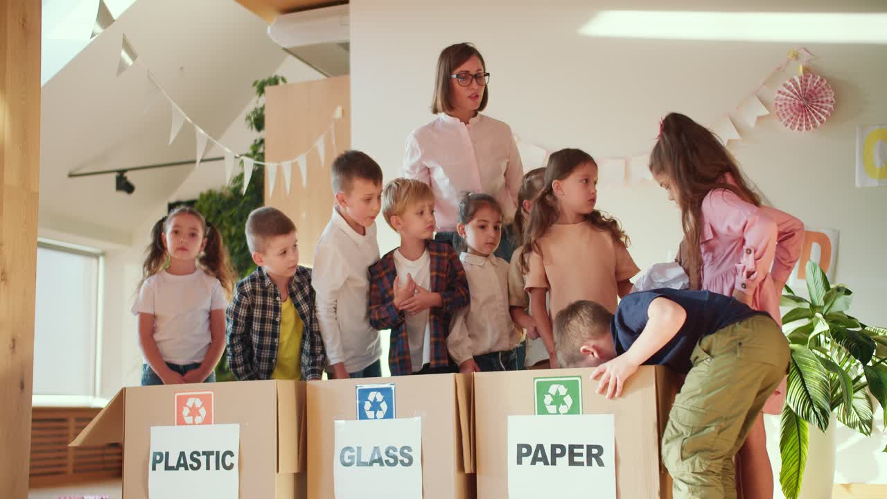 los niños en un club de preparación escolar colocan diferentes tipos de basura en la caja derecha para plástico para vidrio y para papel junto con su maestra, una chica con un bob en una camisa blanca