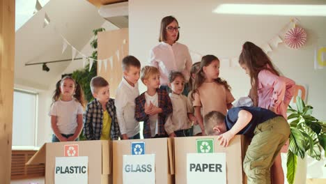 children in a school preparation club lay out different types of garbage in the right box for plastic for glass and for paper together with their teacher, a girl with a bob in a white shirt