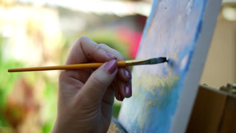 video en cámara lenta de una artista femenina aplicando pintura azul a un lienzo de fondo borroso