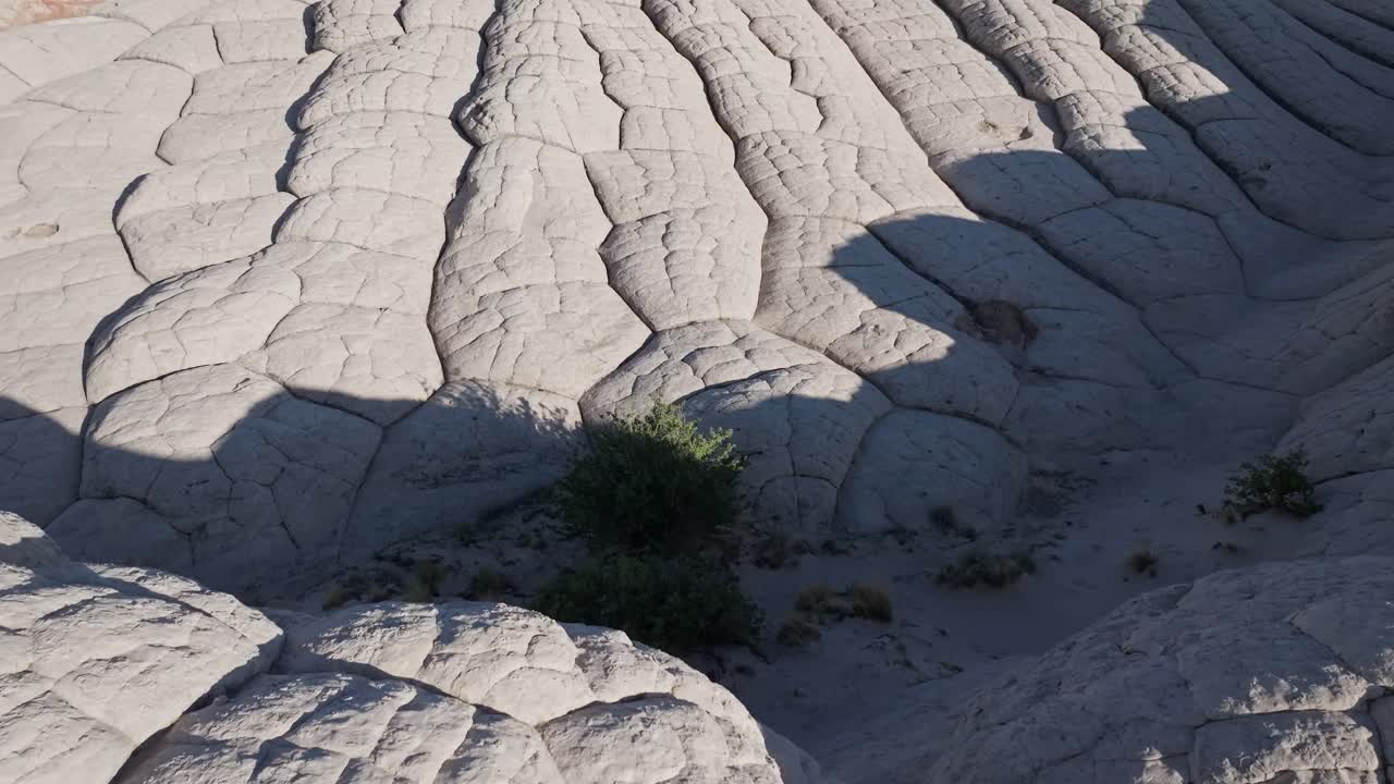A drone flying forward and panning up to reveal two subjects standing on top of the unique sandstone rock features of White Pocket Arizona surrounded by sandy desert and blue skies
