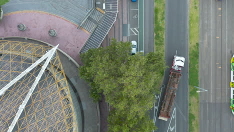 bikes ride along road side while large heavy loading truck passes by a stationary tram