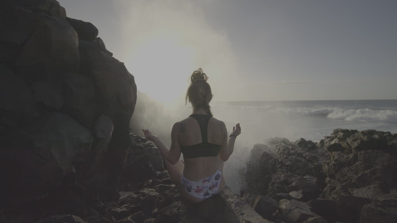 Woman meditating on a rocky beach by the ocean