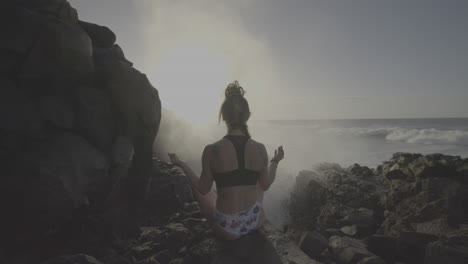 woman meditating on a rocky beach by the ocean