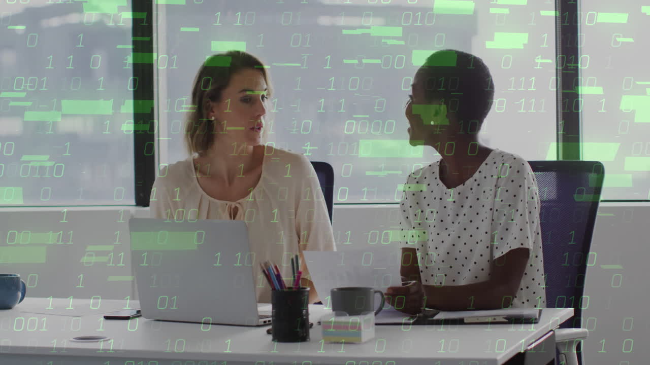 Binary code animation over two women working together at office desk