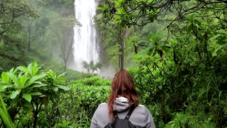 Young-woman-walking-between-tropical-jungle-vegetation-towards-Materuni-waterfall-in-Tanzania