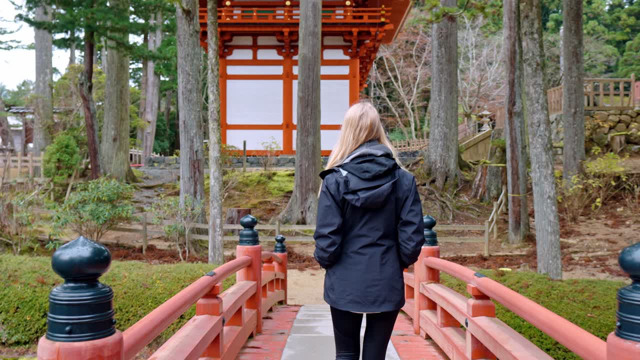 A cinematic scene capturing a blonde girl walking gracefully across a traditional bridge within the sacred grounds of Danjo Garan in Mount Koya, Koyasan, Japan.
