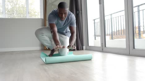 african american man placing yoga mat on floor at home, slow motion