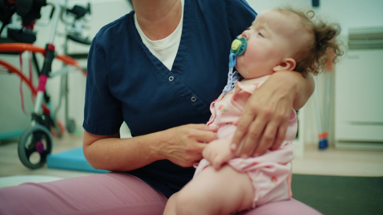 Medical professional helping a crying baby with a pacifier during a pediatric rehabilitation treatment. Developing child support