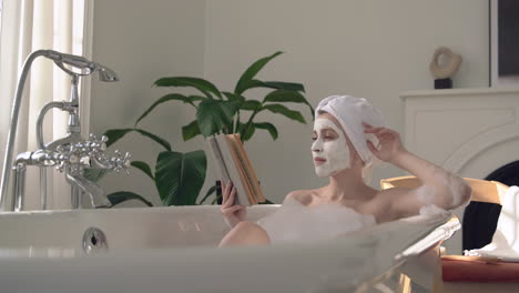 woman with face mask taking a relaxing bath and reading