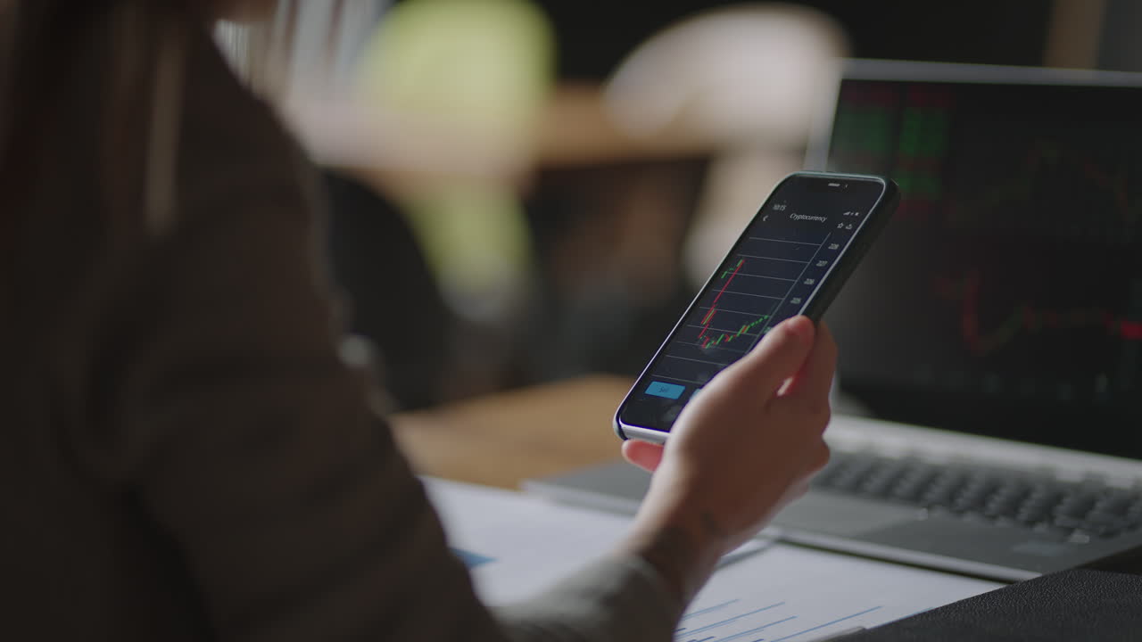 inversionista comprobando los datos del mercado de valores en la pantalla de un teléfono móvil. mujer asiática comerciando en el mercado de valores en un teléfono inteligente con pantalla financiera del mercado de valores. gráfico de precios de criptomonedas en la pantalla de un teléfono inteligente