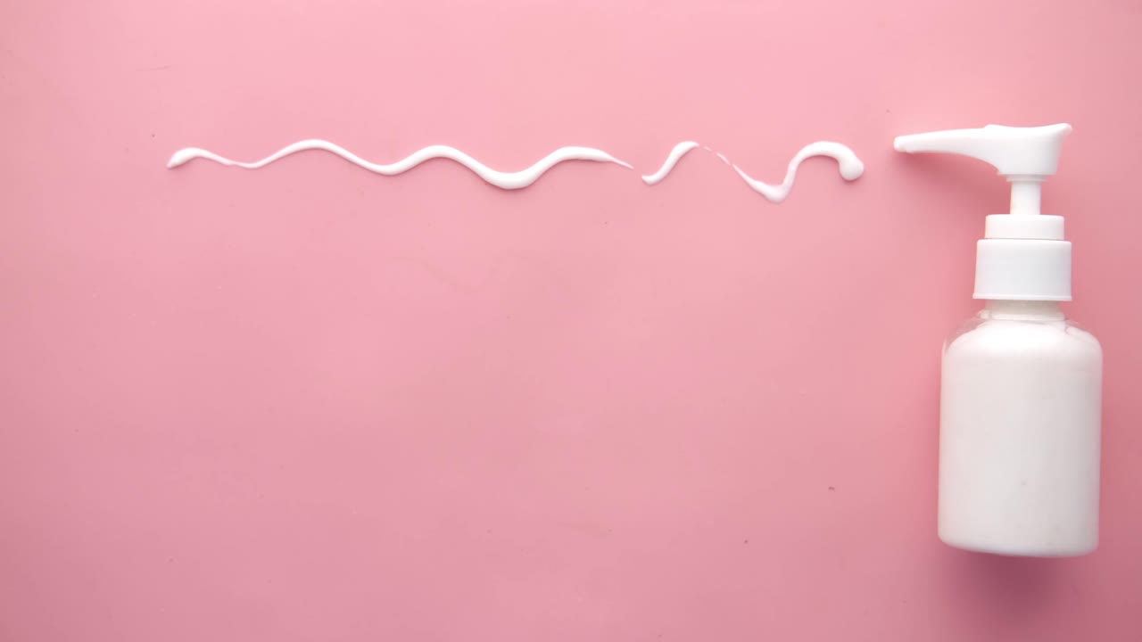 색 로션 병과 분홍색 배경에 스플레이 된 크림