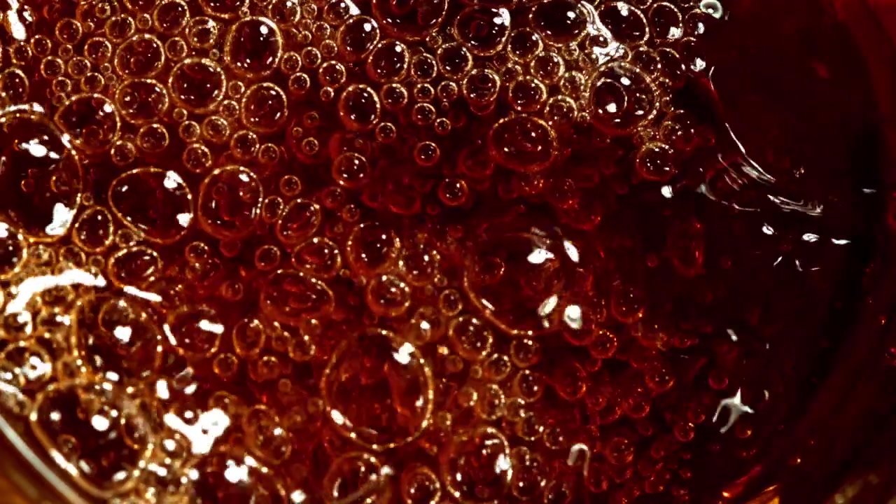 Primo piano di liquido scuro gassato con bollicine e schiuma