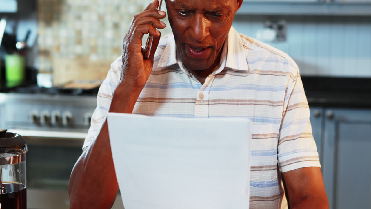 hombre mayor mirando un documento hablando por teléfono móvil