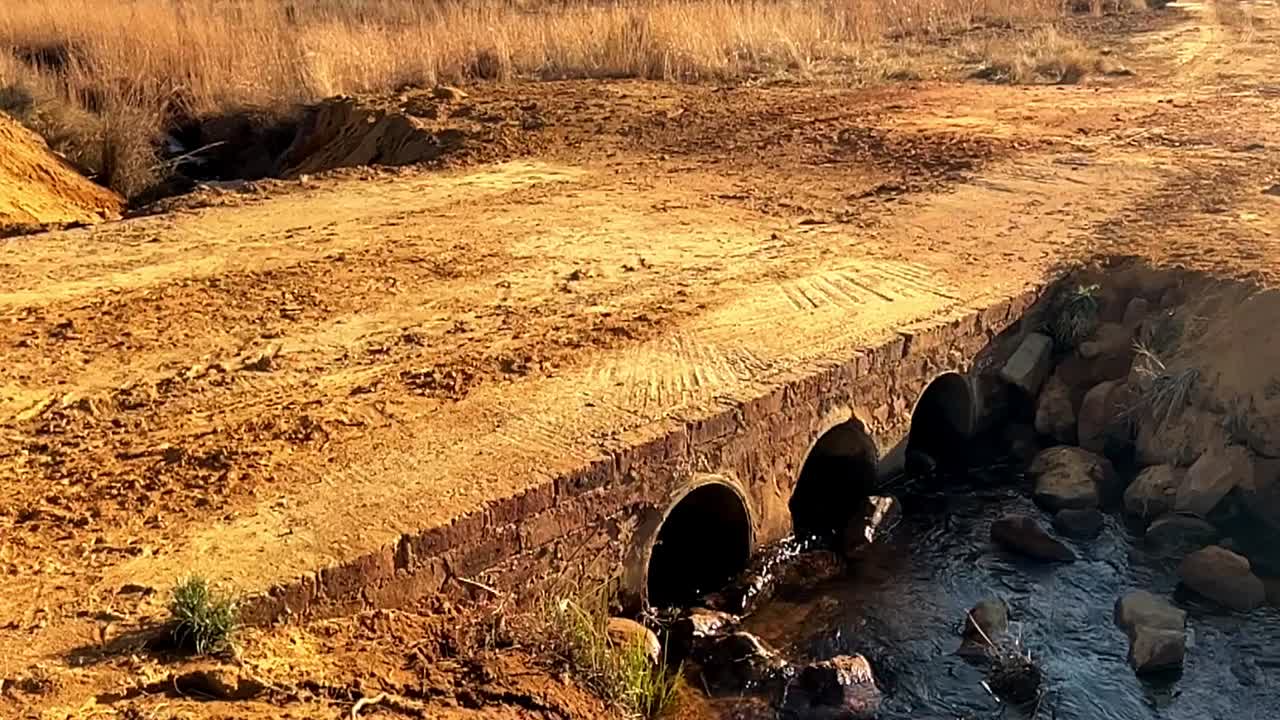 construcción de un puente de paso de agua en una carretera de tierra con tuberías de hormigón, paredes de apoyo y techo de losa sólida