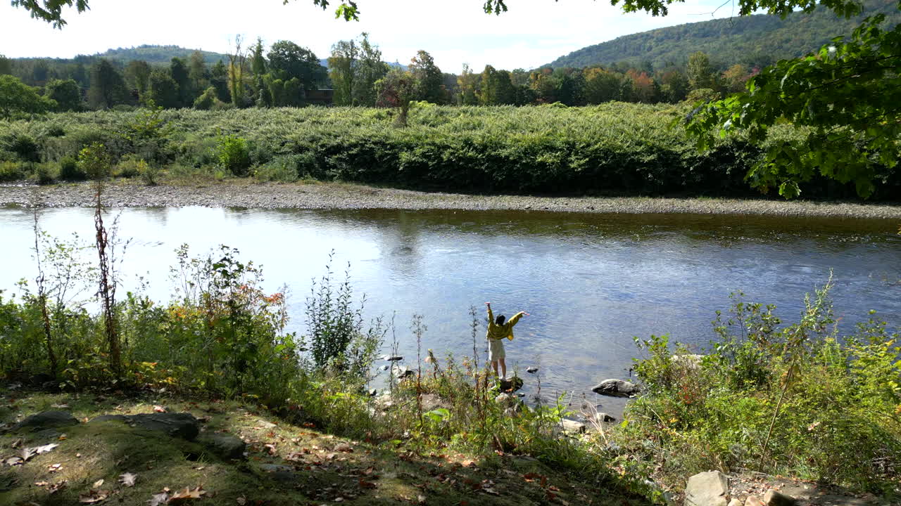 Žena se protahuje, když stojí na břehu vody na stezce Mohawk Trail u řeky Deerfield v západním Massachusetts, Nová Anglie, USA