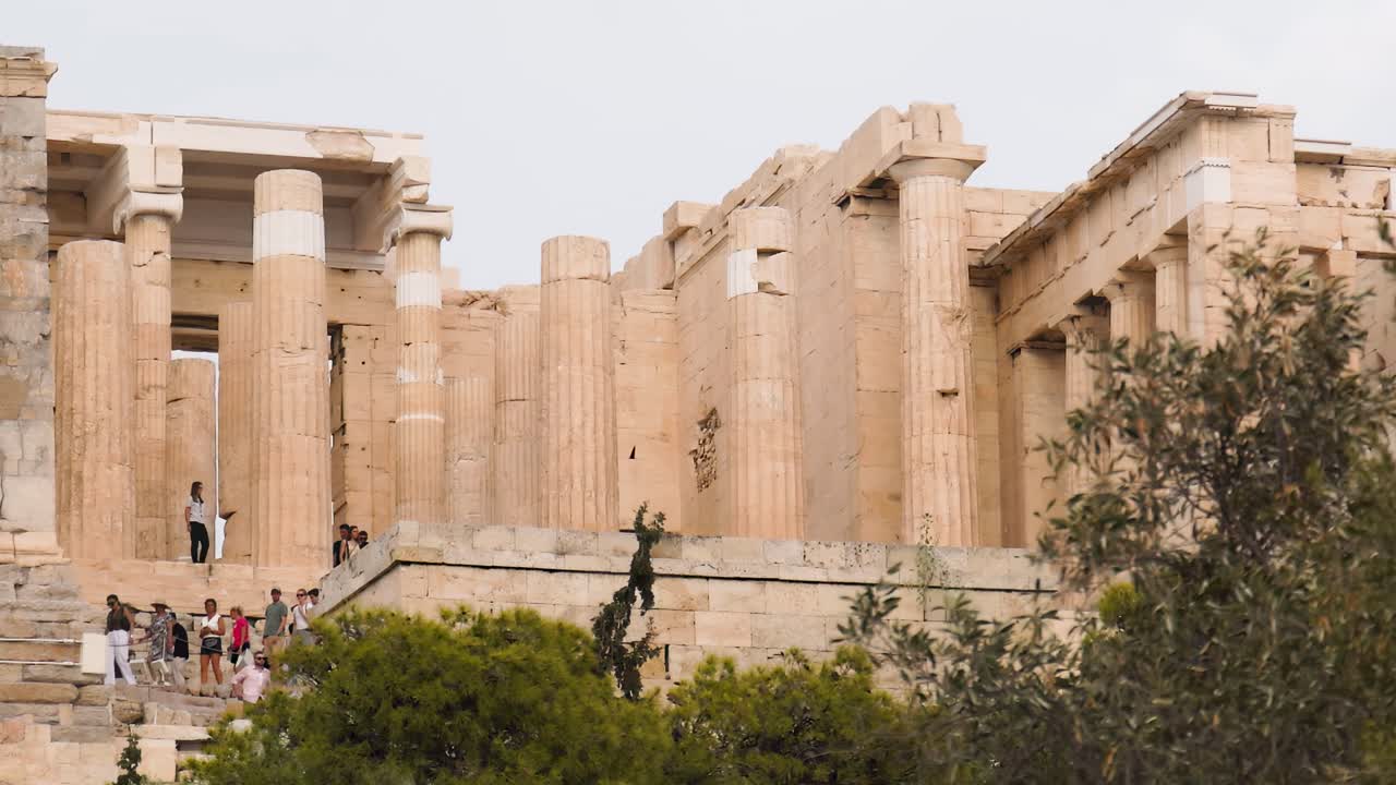 Detailed view of ancient stone columns and architecture surrounded by greenery and visitors.