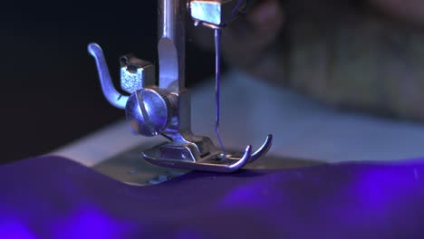 primer plano de una aguja de máquina de coser cosiendo un paño violeta con hilo violeta