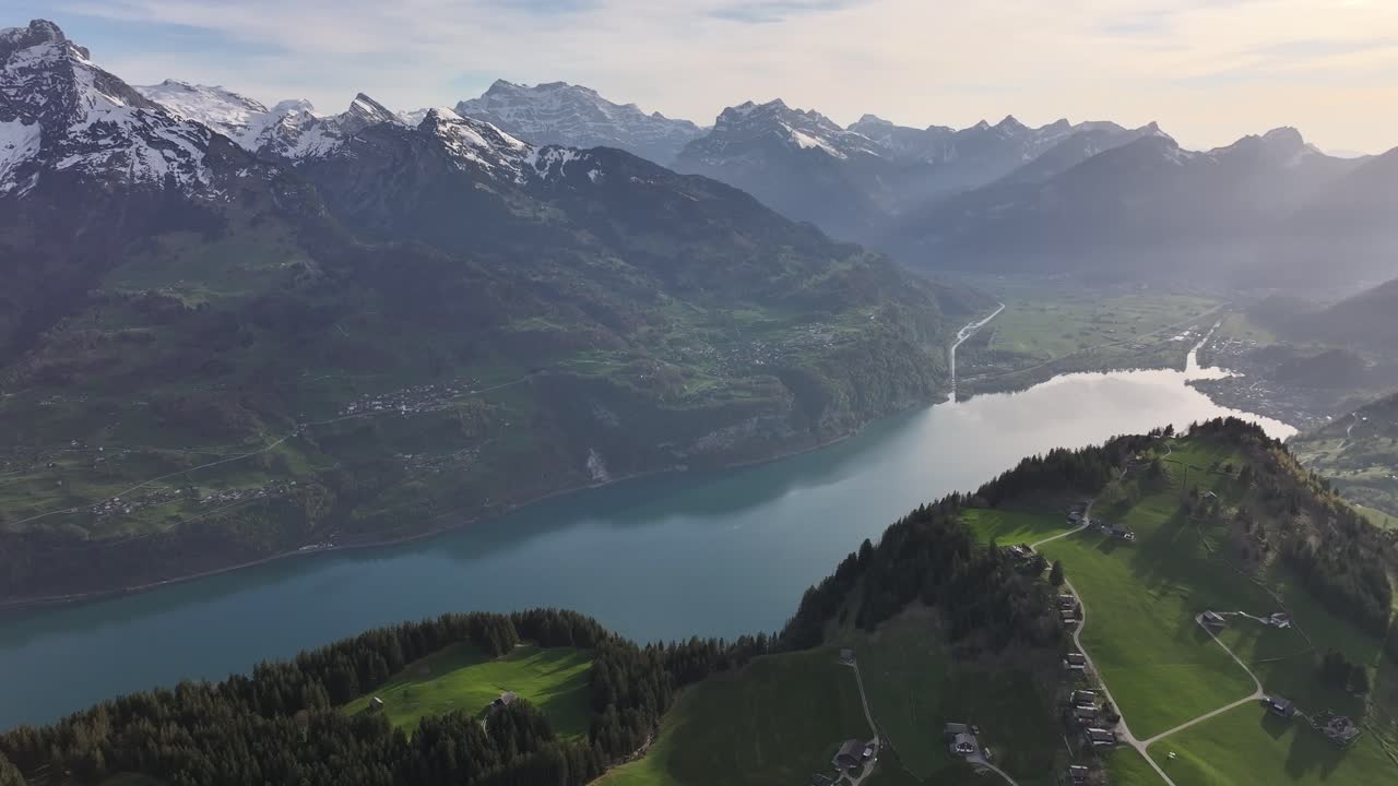 una hermosa toma de avión no tripulado del lago walensee y las aldeas de weesen, amden y quinten en suiza, mostrando cadenas montañosas cubiertas de hielo, parte del lago, colinas verdes, árboles y aldeas