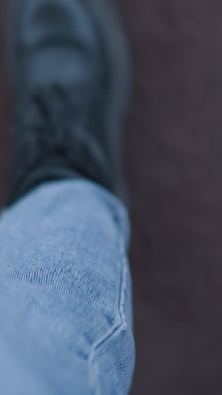 Primo piano delle gambe di una persona con jeans e stivali che trasporta borse della spesa rosa e verde menta su una scala mobile, mentre scende su un tappeto sullo sfondo