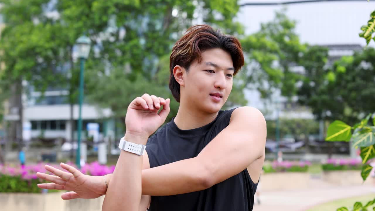 นักกีฬาชายชาวเอเชียยืดกล้ามเนื้อแขนในสวนสาธารณะกลางแจ้งที่สว่างสดใส ภาพระยะกลาง แสงธรรมชาติ