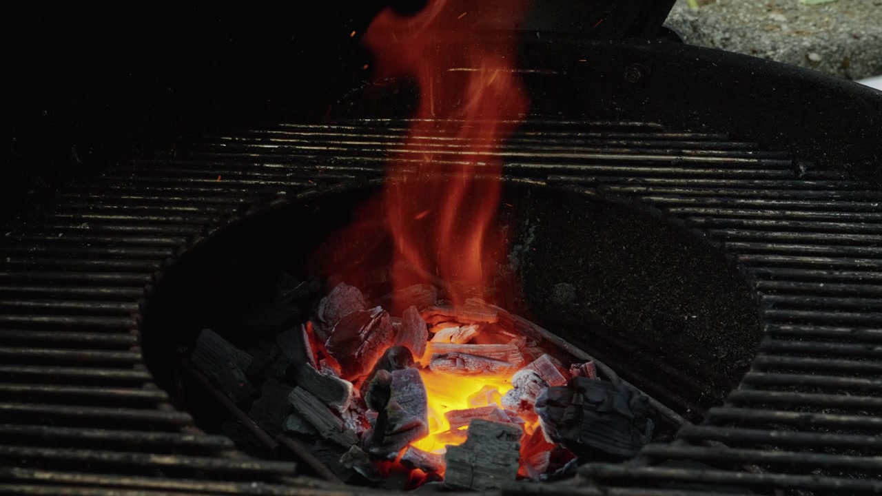 Carboni ardenti e fiamme che si alzano bruciano intensamente al centro di una griglia rotonda per barbecue
