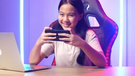 excited asian kid girl playing video game with mobile phone then smiles to camera while live stream