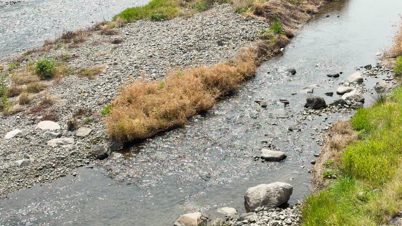Static high-angle shot of clear river water flowing over pebbles and rocks in bright daylight