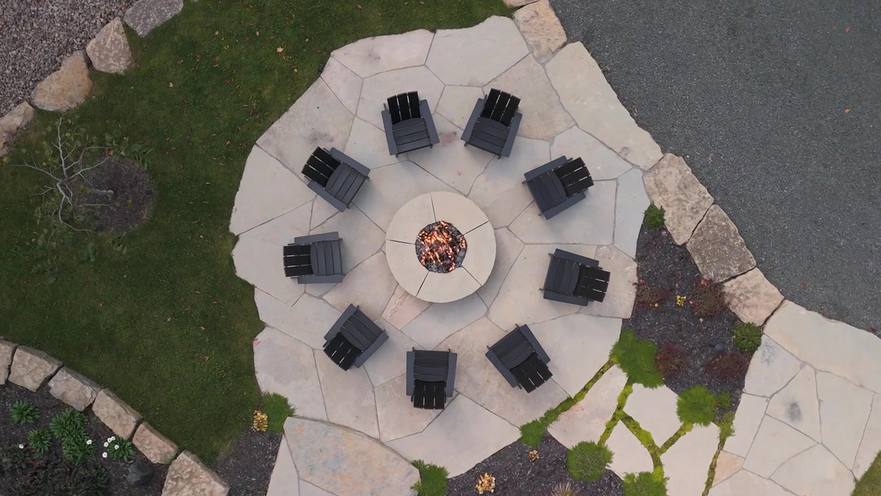 Vista aérea cenital de un dron girando sobre una mesa con fogata al aire libre en un jardín con sendero de piedra y un sofá para reuniones al aire libre en la temporada de otoño e invierno.