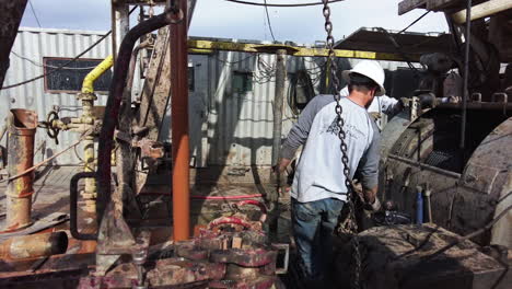 drilling equipment is maintained by the workers wearing helmets. man takes some fuel oil to lubricate the details of equipment.