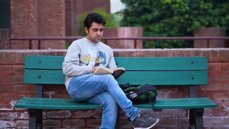 Male-Bookworm-Enjoying-Nature-While-Reading,-Young-South-Asian-Man-Engrossed-in-Reading-Outdoors