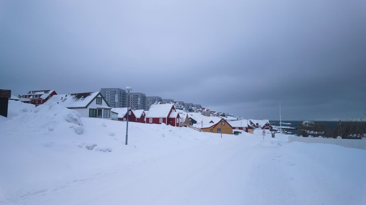 Snowy street with colorful houses by coast in cloudy Nuuk, Greenland