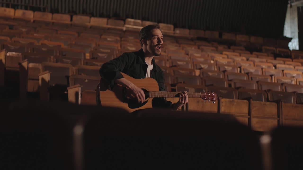 Un bel ragazzo suona una chitarra acustica in un cinema abbandonato. Il musicista canta una canzone e si accompagna con la chitarra