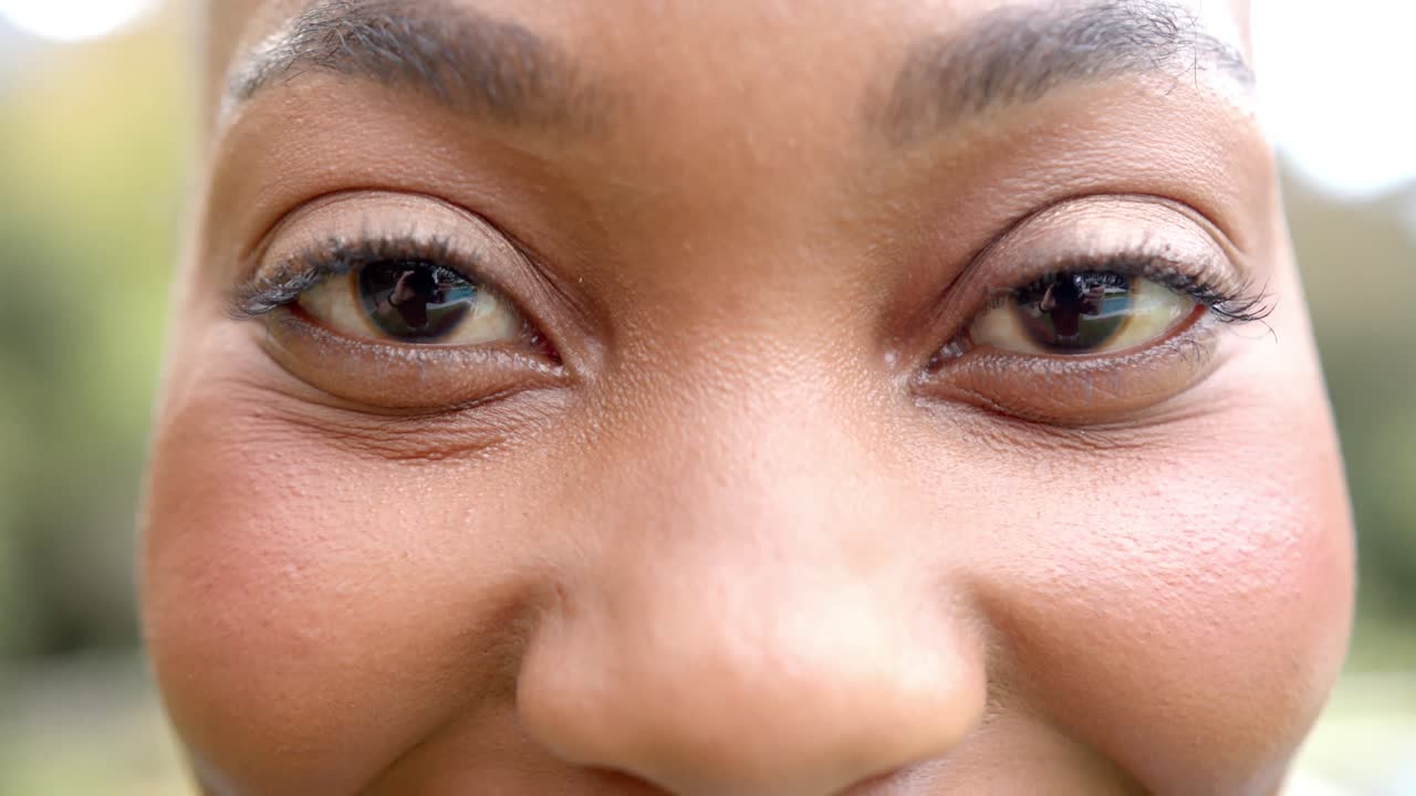 Portrait of close up of eyes of happy african american woman smiling in garden, in slow motion