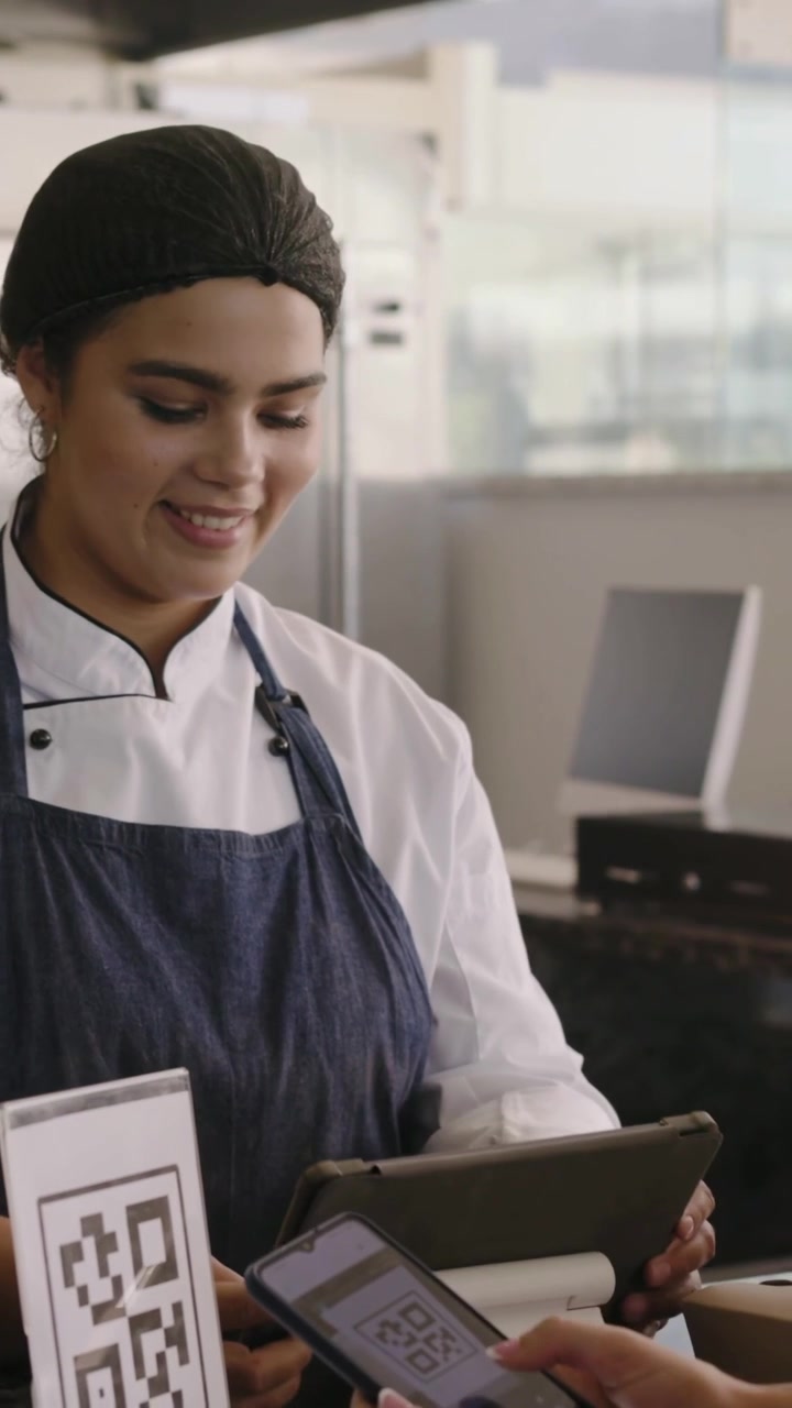 Vídeo vertical: Cliente se aproximando escaneando QR enquanto chef toca no tablet e entrega uma caixa em um café.