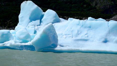 sunlit melting iceberg floating along grey lake, pan left