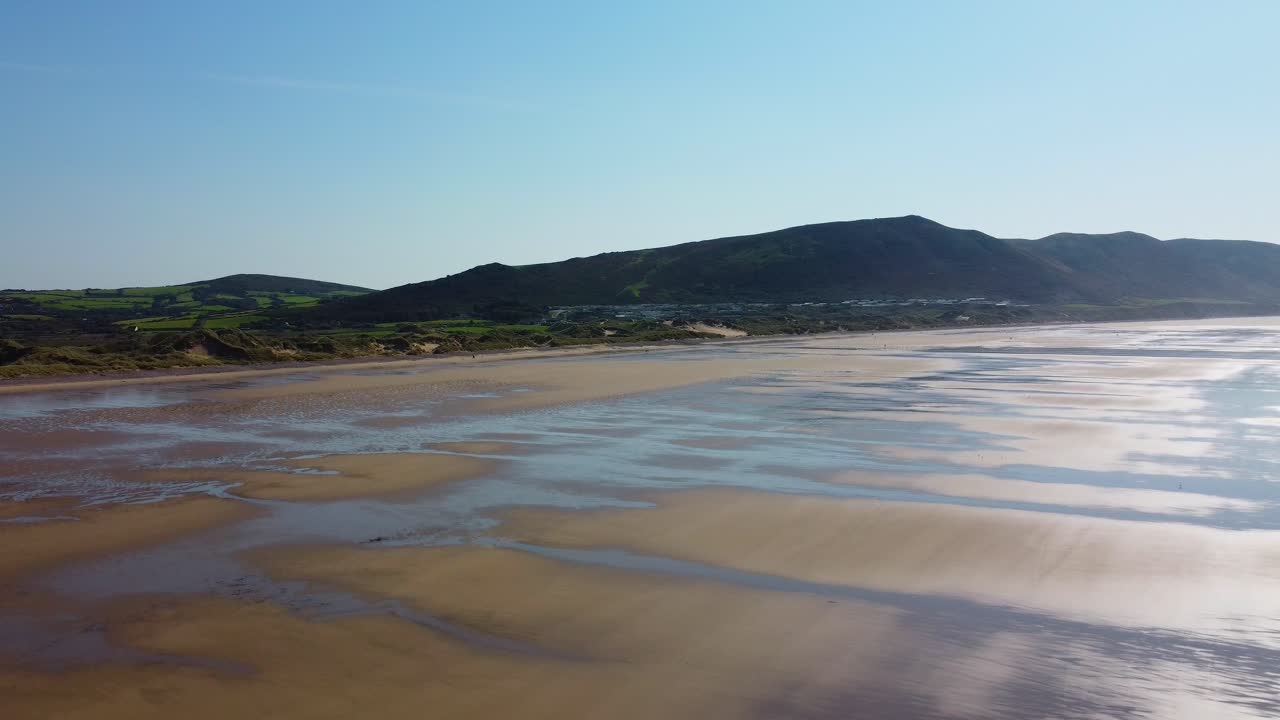 Descending Drone Shot on Rhossili Bay with Grassy Sand Dunes and Moorland Fields Backdrop with Hazy Blue Sky 4K