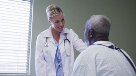 caucasian female doctor talking and supporting african american senior male patient at hospital