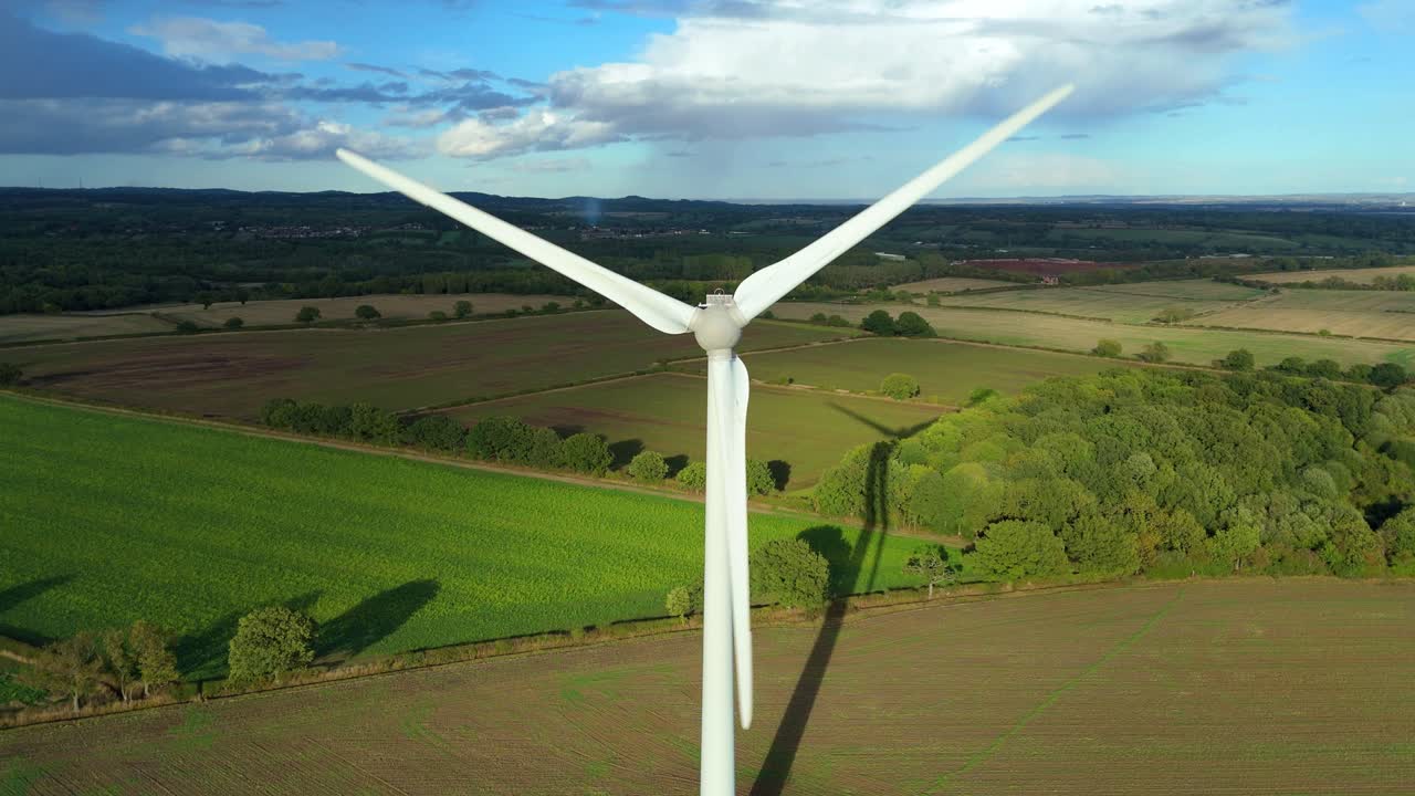 Renewable energy wind turbines spinning across rural landscape and agricultural fields in Leicester, United Kingdom captured by drone