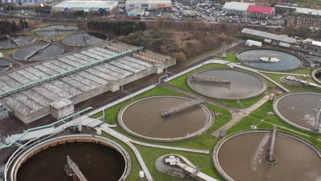 toma aérea gira alrededor de una planta de aguas residuales con cientos de gaviotas dando vueltas y un polígono industrial en el fondo