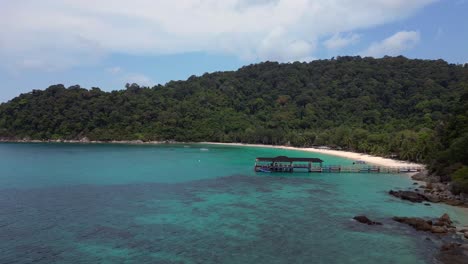 Agua-Turquesa,-Embarcadero-De-La-Playa-De-La-Laguna-En-La-Isla-Besar-Perhentian-Con-Un-Exuberante-Bosque-Tropical-Al-Fondo