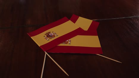 close up of small spain flags on toothpicks laying on a dark reflective wooden table