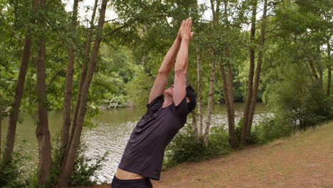 hombre con ropa deportiva haciendo yoga en una alfombra en el bosque junto a un lago o río disfrutando de la paz y la belleza de la naturaleza