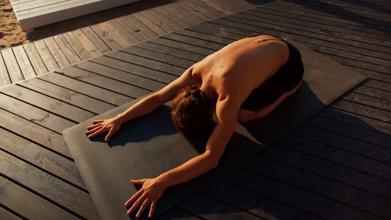 The guy took a special pose for yoga and stretching on a special mat on a sunny beach in the morning