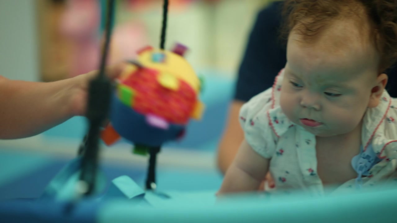 Bebê menina interagindo com um brinquedo de desenvolvimento colorido e brilhante, estimulando o aprendizado sensorial e atividades de fisioterapia.